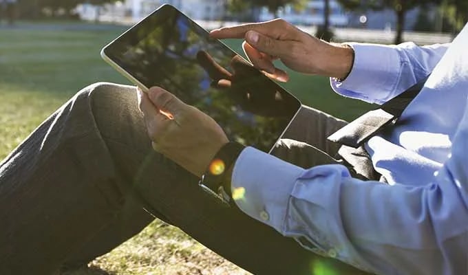 Hombre revisa sus ahorros a través de una tablet, sentado en un parque